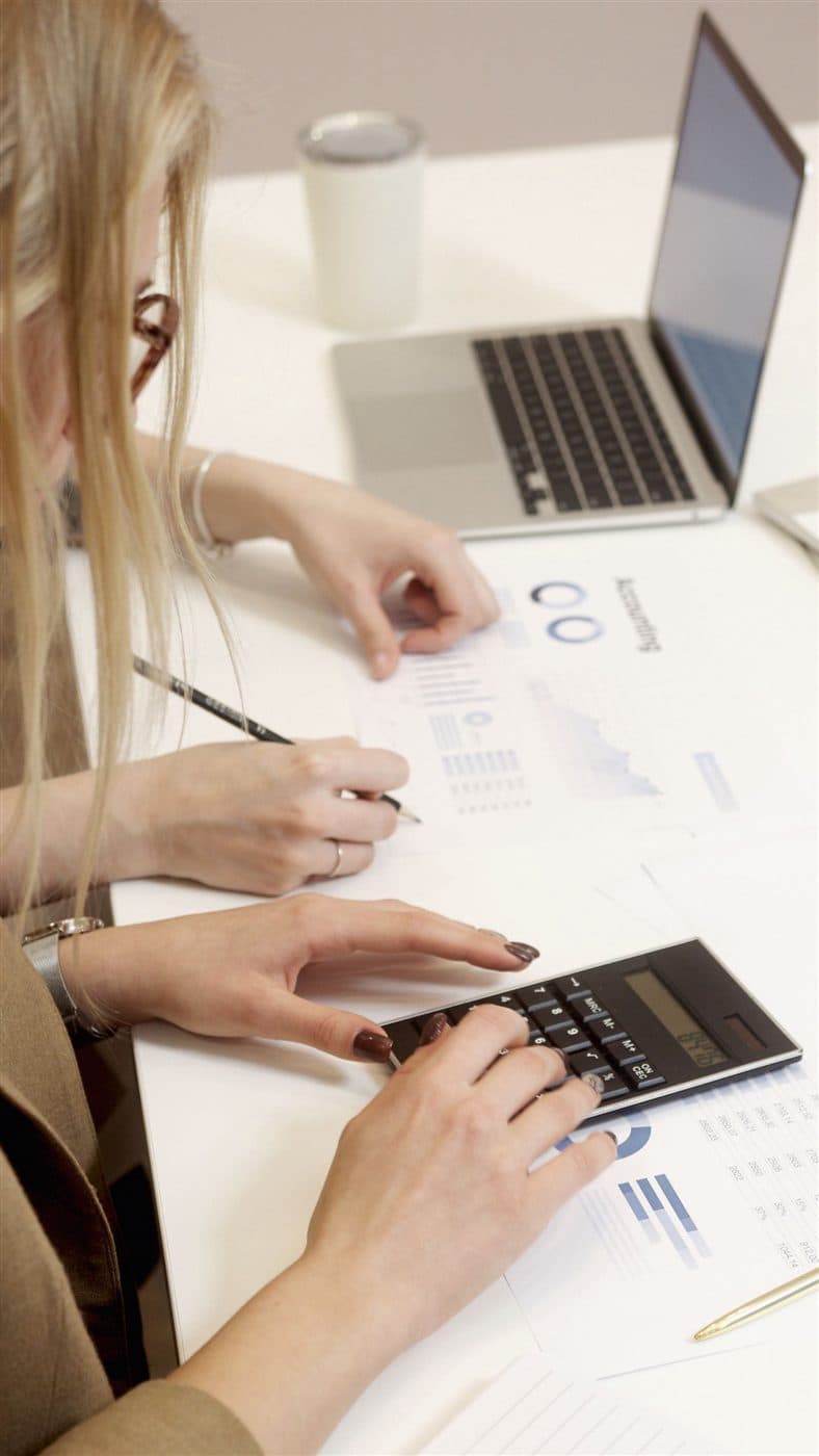 Profissional analisa relatórios financeiros com gráficos, calculadora e notebook.